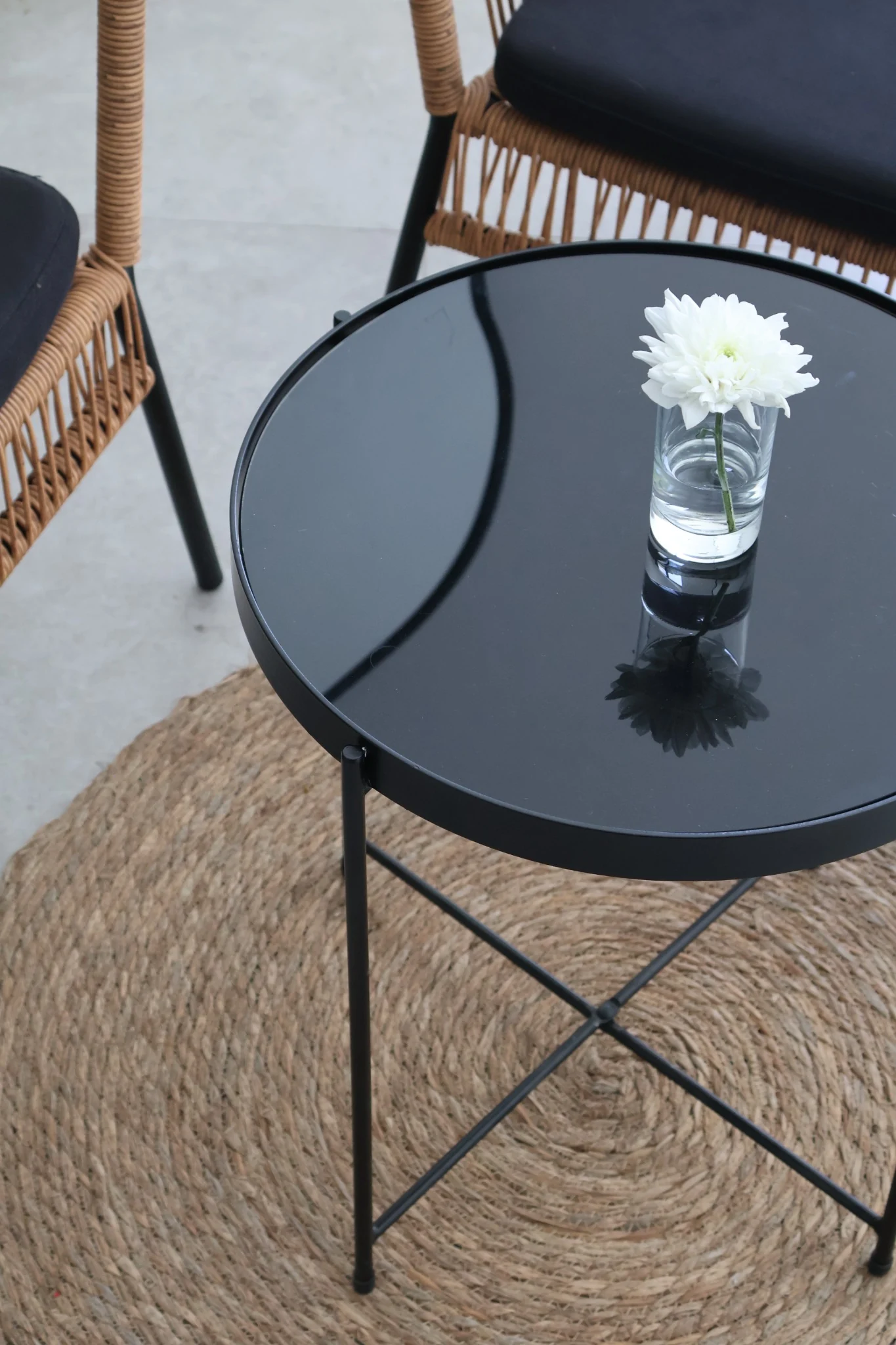Piccolo vaso in vetro con fiore bianco su un tavolo nero lucido.
